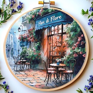 May include: A painting depicting a Parisian cafe with a blue awning that reads "Fleure de Flore". The cafe is surrounded by lush greenery and has a few tables and chairs set up outside.