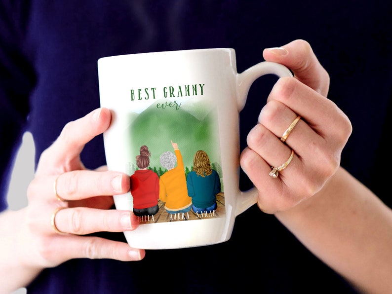 May include: White ceramic mug with a green mountain scene and three women standing in front of it. The mug says "Best Granny ever" and has the names "Hilla, Audra, Sarah" at the bottom.