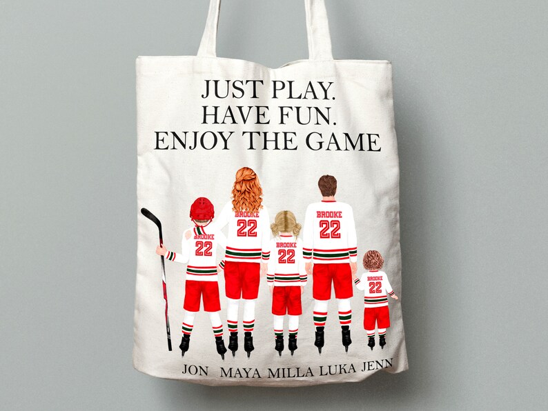 May include: A white canvas tote bag with the text "JUST PLAY. HAVE FUN. ENJOY THE GAME" printed on the front. The bag features a family of five wearing hockey jerseys with the number 22 and the name "BROOKE" printed on the back. The names "JON, MAYA, MILLA, LUKA, JENN" are printed at the bottom of the bag.