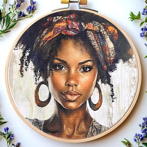 Puede incluir: Un retrato de punto de cruz de una mujer de piel oscura, que lleva un pañuelo estampado y pendientes de aro grandes. La obra de arte está enmarcada en un bastidor de bordado de madera, con un fondo blanco y gris claro. La imagen está rodeada de ramitas de flores moradas.