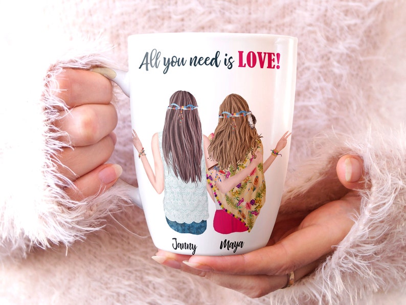 May include: White ceramic mug with a graphic of two women with long hair wearing headbands. The text "All you need is LOVE!" is printed on the mug. The names "Janny" and "Maya" are printed below the women.