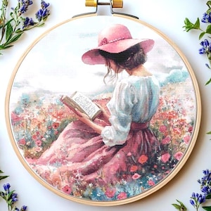 Könnte beinhalten: Eine Frau in einem rosa Kleid und Hut sitzt auf einem Feld voller Blumen und liest ein Buch. Die Blumen sind in den Farben Rosa, Lila und Weiß.