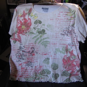 May include: A cream-colored short-sleeved shirt with a floral design in red, green, and gray. The shirt has a scoop neck and a scalloped hem. The text "EDITIONS" is visible on the label.