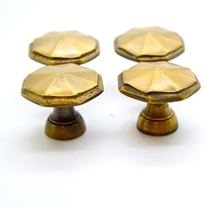 Könnte beinhalten: Vier antike Messing-Schrankknöpfe mit achteckigem Design. Die Knöpfe haben eine warme, gealterte Oberfläche und sind vor einem weißen Hintergrund platziert. Jeder Knopf hat einen Durchmesser von ca. 3,8 cm und ist 2,5 cm hoch.