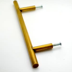 May include: A gold-toned metal cabinet pull with a straight bar design and two screws.