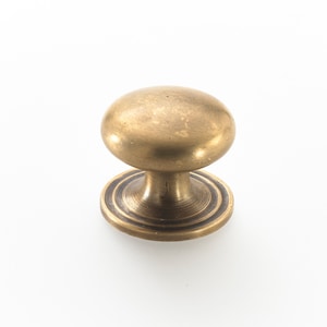 May include: A brass cabinet knob with a round, slightly domed top and a circular base with a decorative ring.