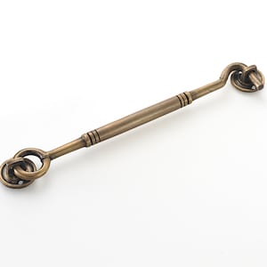 May include: Antique brass door hook with a looped handle and a round base. The hook is designed to be mounted on a door or wall.