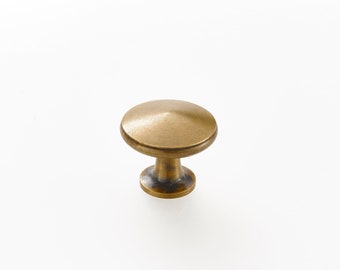May include: A single, antique brass cabinet knob. The knob has a rounded top and a short, cylindrical base. The finish is a warm, aged brass color, suggesting a vintage or rustic aesthetic. The knob is designed for use on drawers or cabinet doors.