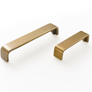 May include: Two brushed brass cabinet pulls with a rectangular shape and rounded edges. The larger pull is approximately 5 inches long and the smaller pull is approximately 3 inches long.