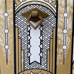 May include: A gold-colored metal door pull with a diamond-shaped design. The pull is set against a background of black and white geometric patterns.