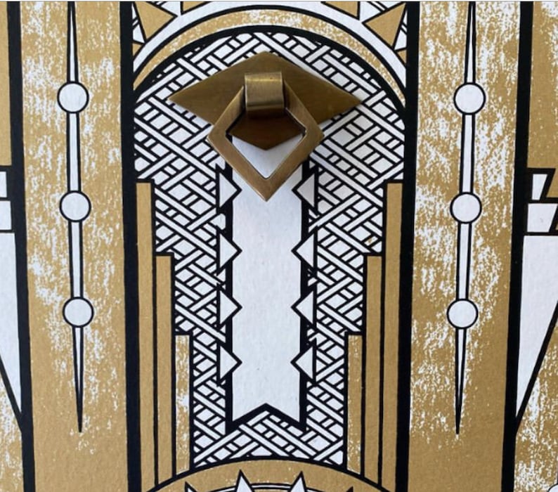 May include: A gold-colored metal door pull with a diamond-shaped design. The pull is set against a background of black and white geometric patterns.