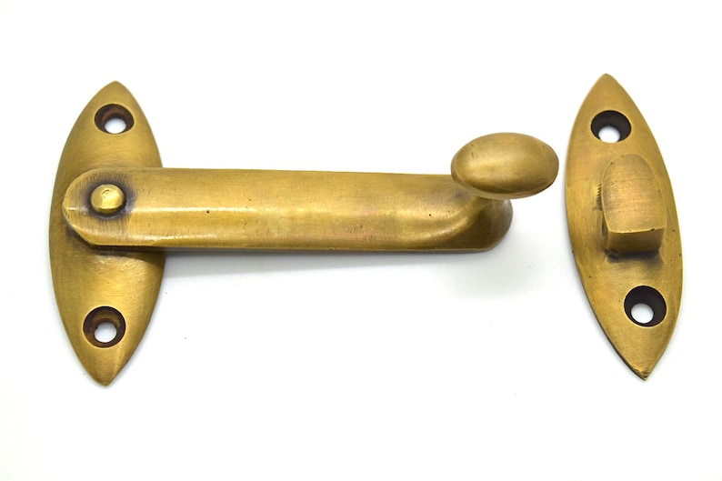 May include: A brass window sash lock set against a white background. The set includes two oval-shaped pieces with screw holes and a pivoting arm with a rounded handle. The metal has a warm, aged finish.