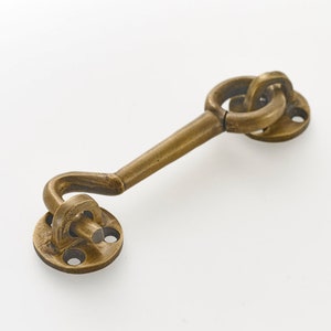 May include: A brass door hook with a curved hook and a round base. The hook is attached to a round plate with three holes.
