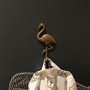 May include: A bronze flamingo hook mounted on a dark wall, holding a white towel with a black dog print and a black and white striped towel. The hook is a decorative accent.
