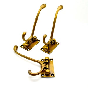 May include: Three antique brass coat hooks. Each hook has a curved design and is mounted on a rectangular base with screw holes. The hooks are a warm, golden color, suggesting an aged finish. Ideal for entryways or closets.