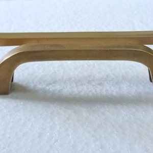 Peut inclure: Deux poignées de cabinet de couleur or avec un design arqué. La plus petite poignée est au-dessus de la plus grande.