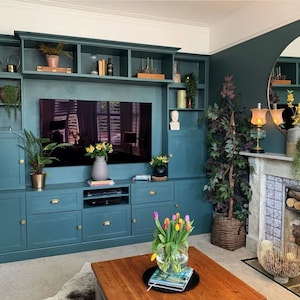 May include: A teal green entertainment center with a built-in television, shelves, and cabinets. The entertainment center is in a living room with a fireplace and a large round mirror.