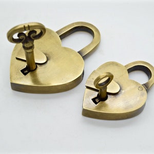 May include: Two heart-shaped brass padlocks with keys inserted. The padlocks are in different sizes, with a key inserted in each lock. The keys have ornate, decorative tops. The padlocks are on a white background.