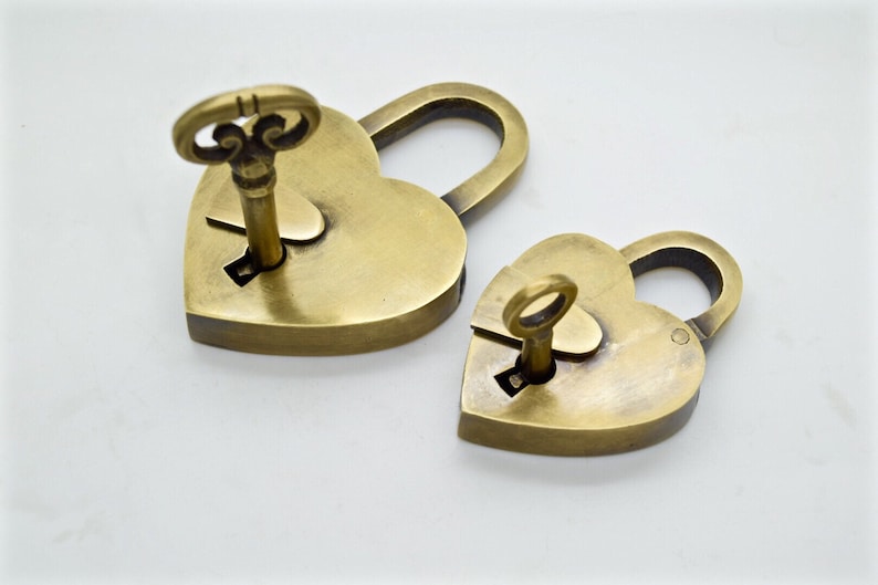 May include: Two heart-shaped brass padlocks with keys inserted. The padlocks are in different sizes, with a key inserted in each lock. The keys have ornate, decorative tops. The padlocks are on a white background.