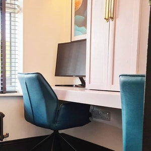 May include: A white desk with a black computer monitor and two teal blue office chairs. The desk is mounted to the wall and has a white cabinet above it. The cabinet has two doors with gold handles.
