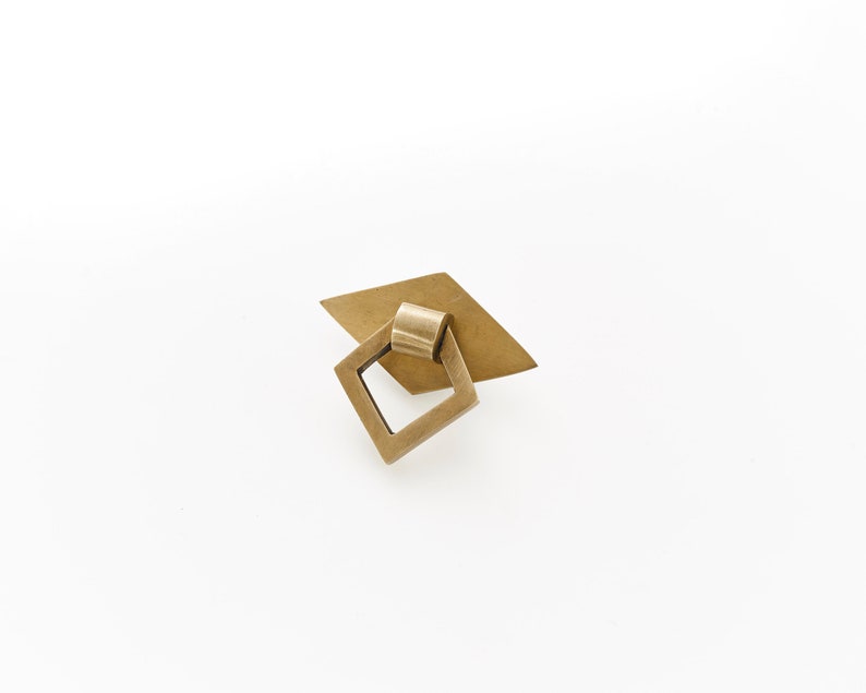 May include: A brass cabinet pull with a diamond-shaped base and a square ring pull.