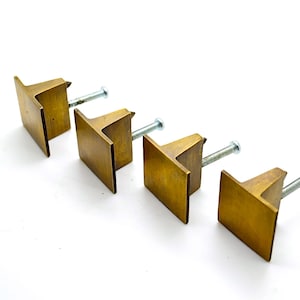 May include: Set of four square brass cabinet knobs with a brushed finish and silver screws.