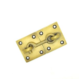 May include: Brass door latch with a hook and eye design. The latch is attached to two square plates with four holes each.
