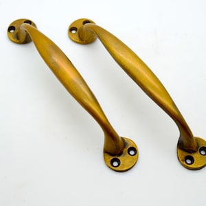 May include: Two antique brass door handles with a curved design. The handles have three holes for mounting.