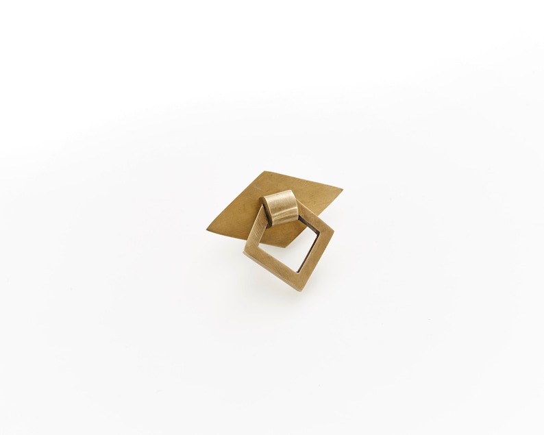 May include: A brass cabinet pull with a square ring and a diamond-shaped base.