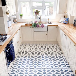 May include: A white kitchen with wood countertops and white cabinets. The floor is tiled with a black and white geometric pattern. There is a window with a view of a garden.