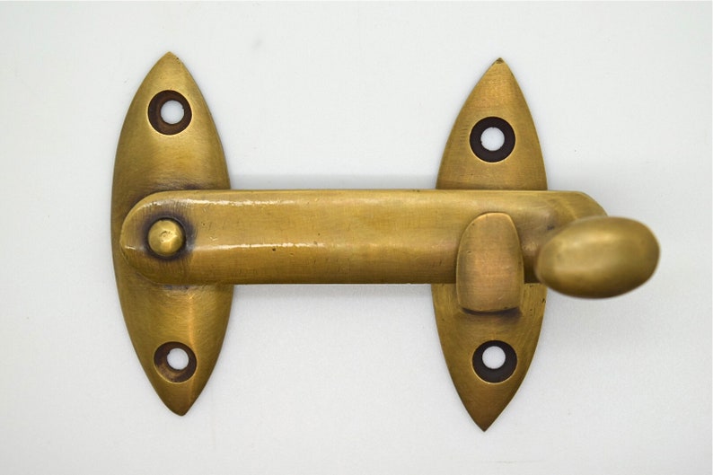May include: A brass-toned cabinet latch with an oval handle and two pointed, oval-shaped mounting plates. Each plate has two screw holes. The latch is designed to secure a cabinet door or drawer.