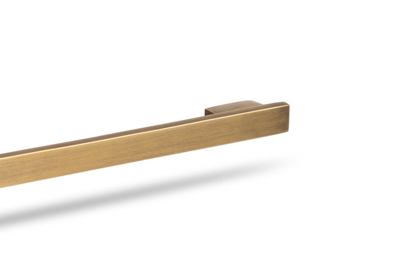 May include: A brushed gold cabinet pull with a rectangular shape.