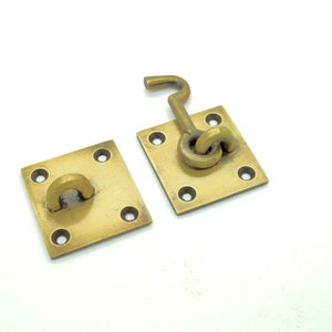 May include: Two brass door latch plates with a square shape and four holes. One plate has a hook latch attached to it.