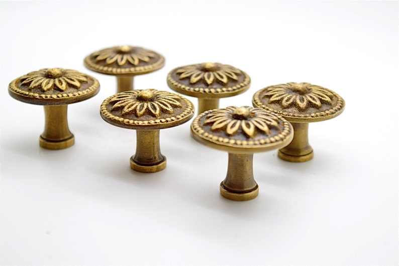 May include: Six antique brass cabinet knobs with a floral design. Each knob has a round base and a raised, detailed flower pattern.