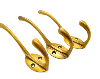 May include: Three antique brass hooks with a curved design and oval bases. Each hook has two small holes in the base.