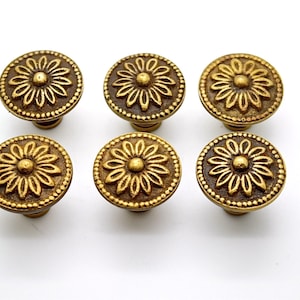 May include: Six gold-toned cabinet knobs with a floral design. Each knob features a raised, circular flower with a central dot.