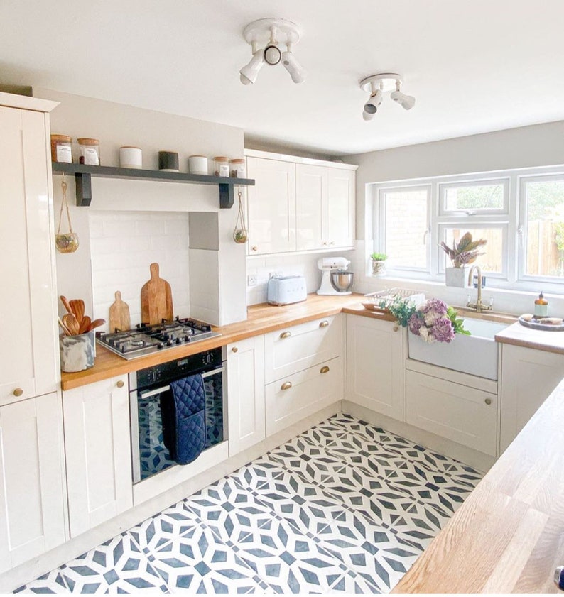 May include: A white kitchen with white cabinets, wood countertops, and a black and white patterned tile floor. The kitchen features a white farmhouse sink, a gas stove, and a black oven.