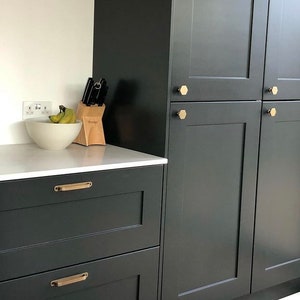 May include: A dark green kitchen cabinet with two drawers and a set of upper cabinets. The drawers have brushed gold handles. The upper cabinets have hexagonal brushed gold knobs. The cabinet is in a modern kitchen.