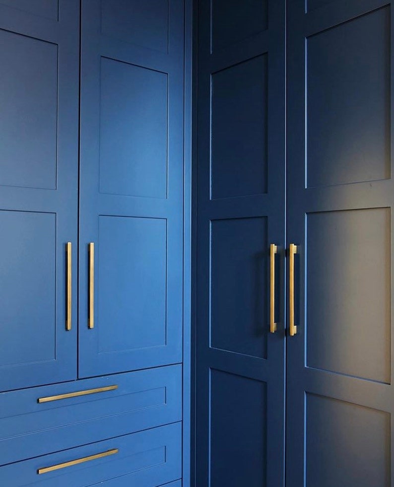 May include: Close-up of a set of blue closet doors with gold hardware. The doors have a raised panel design and are accented with gold pulls.