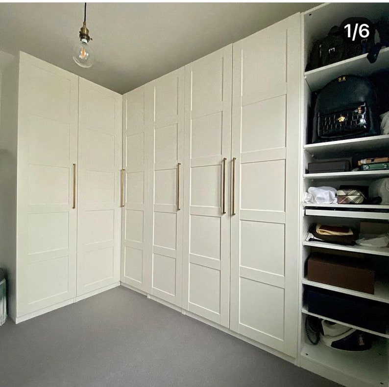 May include: A set of white closet doors with gold handles. The doors are arranged in a corner and have a simple, modern design.