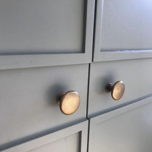 May include: Close-up of two cabinet doors with a light gray paint finish. Each door has a round, brass knob.