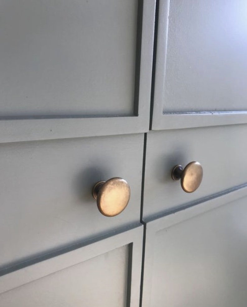 May include: Close-up of two cabinet doors with a light gray paint finish. Each door has a round, brass knob.