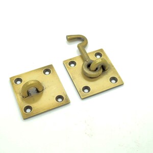 May include: Two brass door latch plates with a square shape and four holes. One plate has a hook latch attached to it.
