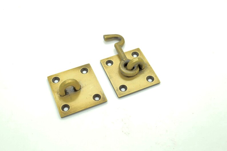 May include: Two brass door latch plates with a square shape and four holes. One plate has a hook latch attached to it.