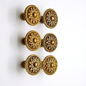 May include: Six gold-toned metal knobs with a floral design. Each knob has a round base and a raised floral pattern.