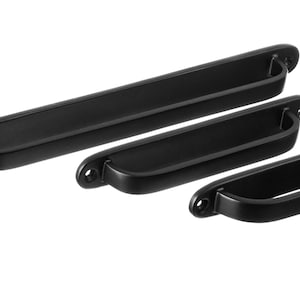 May include: Three black metal drawer pulls of varying sizes. The pulls have a slightly curved, rectangular shape with rounded edges.