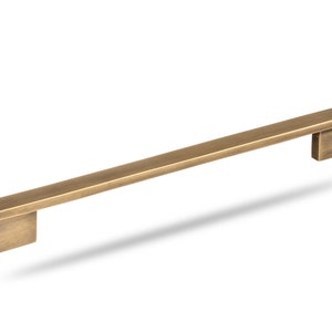 May include: A brushed brass cabinet pull with square ends. The pull is approximately 12 inches long.