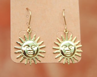 May include: Gold sun face dangle earrings on a brown card with the text "Bo & Ho" written in black ink.