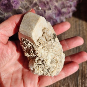 May include: A white, rough-textured crystal cluster with a large, clear crystal in the center. The crystal is surrounded by smaller, white crystals.