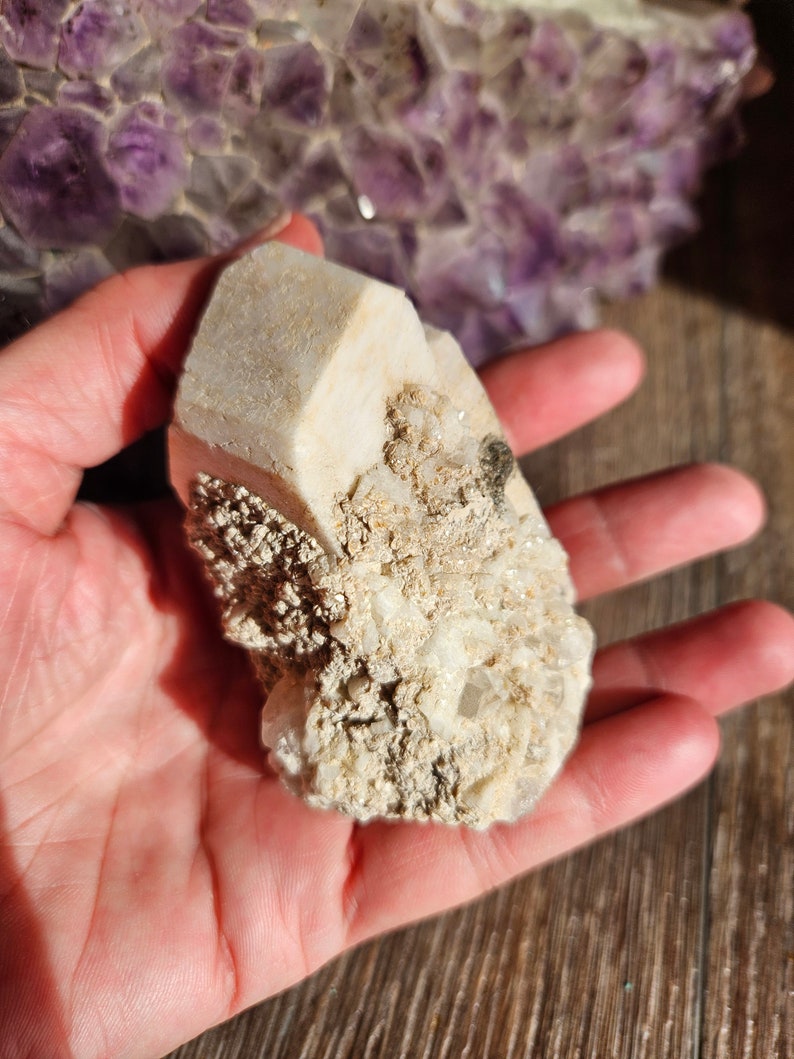 May include: A white, rough-textured crystal cluster with a large, clear crystal in the center. The crystal is surrounded by smaller, white crystals.